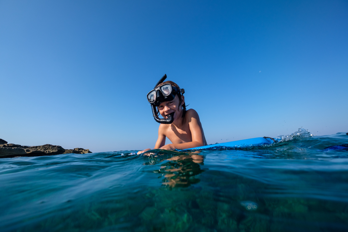 Happy preteen boy in snorkeling mask preparing for diving in blue seawater in sunny cloudless day